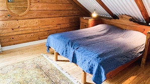 Ein Schlafzimmer einer Holzhütte mit einem Bett, einem Nachttisch, einem Spiegel und einer Pendelleuchte.