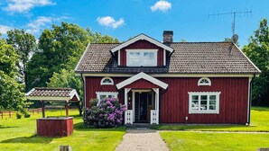 Ein rotes Holzhaus mit weißem Veranda, einem kleinen Garten und einem weißen Zaun.