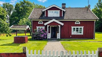 A red wooden house with a white porch, a small garden, and a white picket fence.