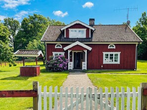 A red wooden house with a white porch, a small garden, and a white picket fence. - 9 Person Holiday Home in Almhult (Almhult)