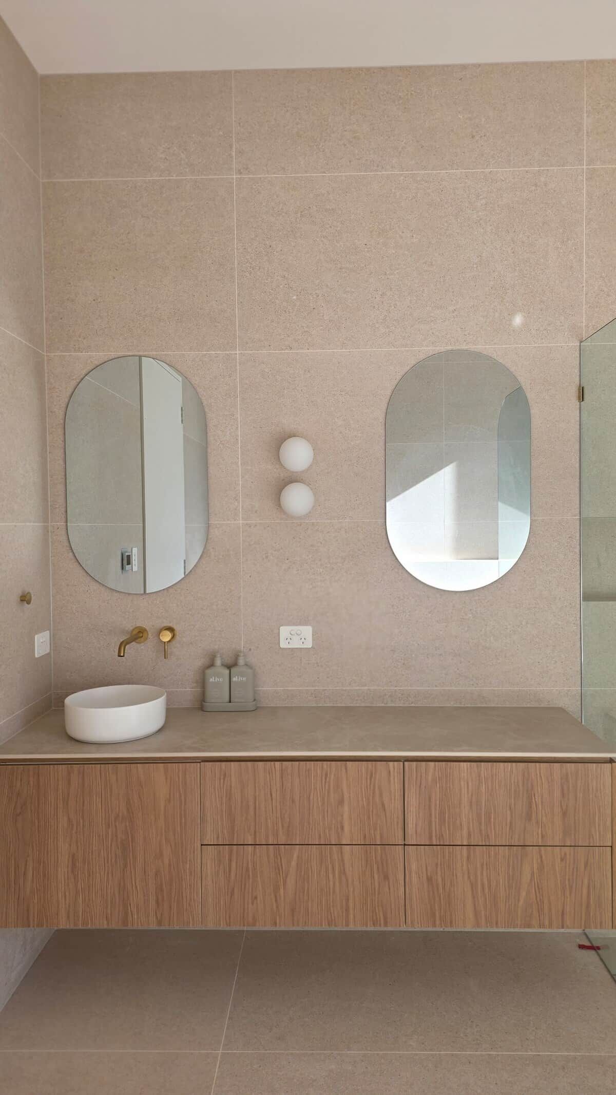 Une salle de bain moderne avec deux grands miroirs, un lavabo rond et un meuble-lavabo en bois.