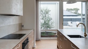 Una cocina moderna con armarios de madera, una estufa negra y un amplio ventanal con vista a un árbol y un edificio.