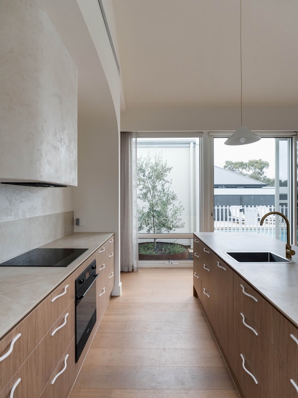 A modern kitchen with wooden cabinets, a black stove, and a large window with a view of a tree and building.