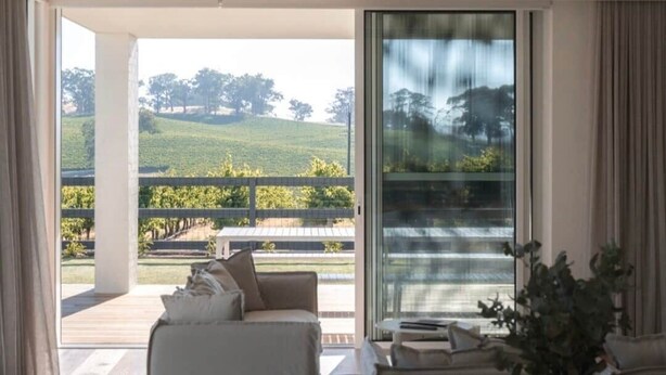 Una habitación con un gran ventanal corredera que da a un espacio exterior con vistas a un viñedo.