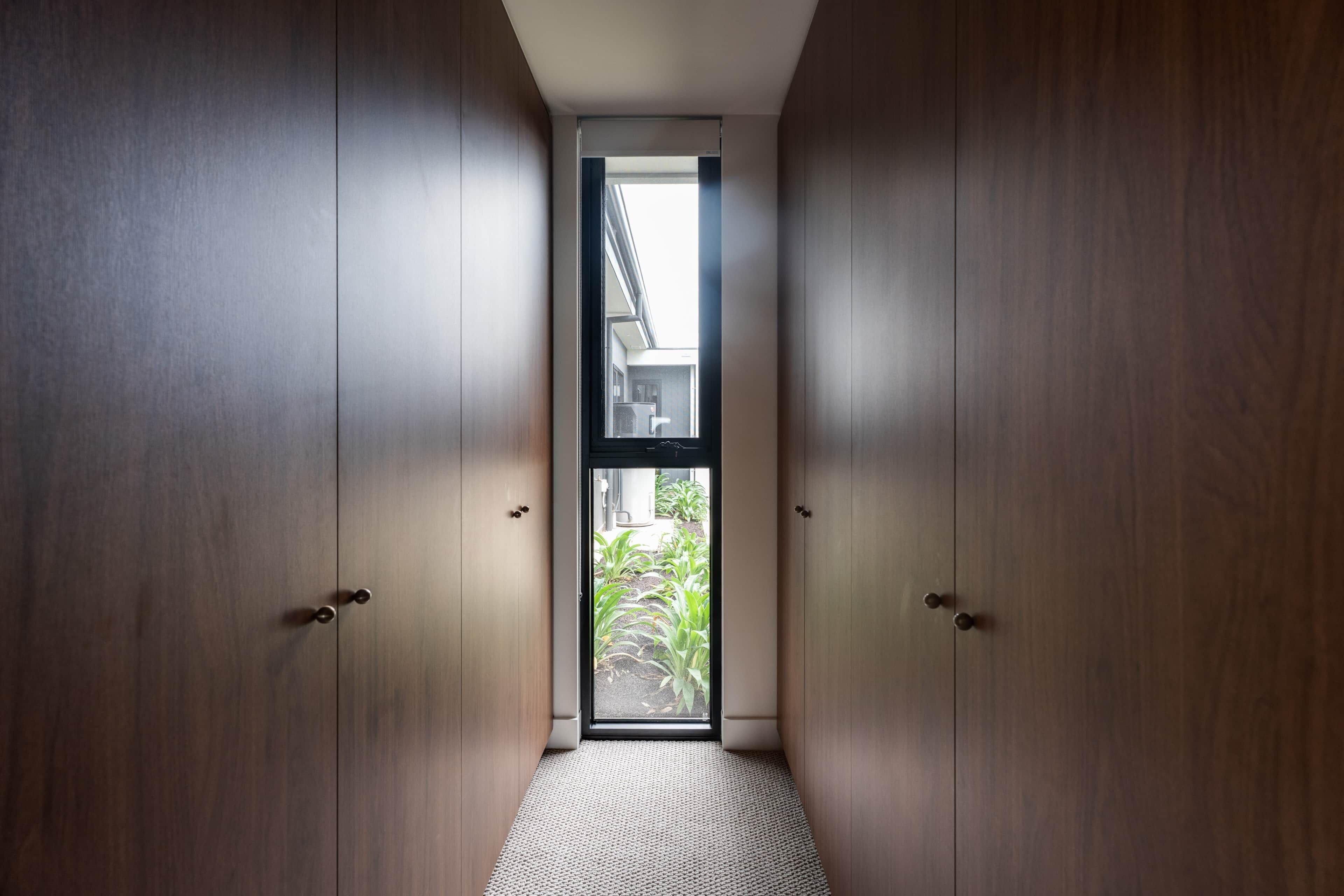 A narrow hallway with wooden doors and a small window at the end.