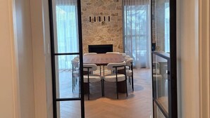 Un couloir mène à une salle à manger agrémentée d’un mur en pierre, d’une cheminée et d’une table ronde entourée de chaises.
