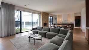 Un salon moderne avec un canapé d’angle, une table basse et une vue sur la ville grâce à de grandes fenêtres.