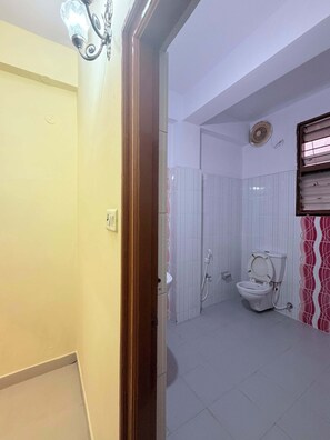 A bathroom with a toilet, shower, and a wall-mounted fan. - Home roots service apartment provide comfort zone long staying client (Hyderabad)