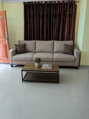 A living room with a sofa, a coffee table, a door, and a curtain. - Home roots service apartment provide comfort zone long staying client (Hyderabad)