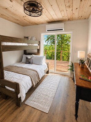 Un dormitorio con literas, un escritorio, una silla, una lámpara y vistas a la vegetación a través de una puerta corrediza.