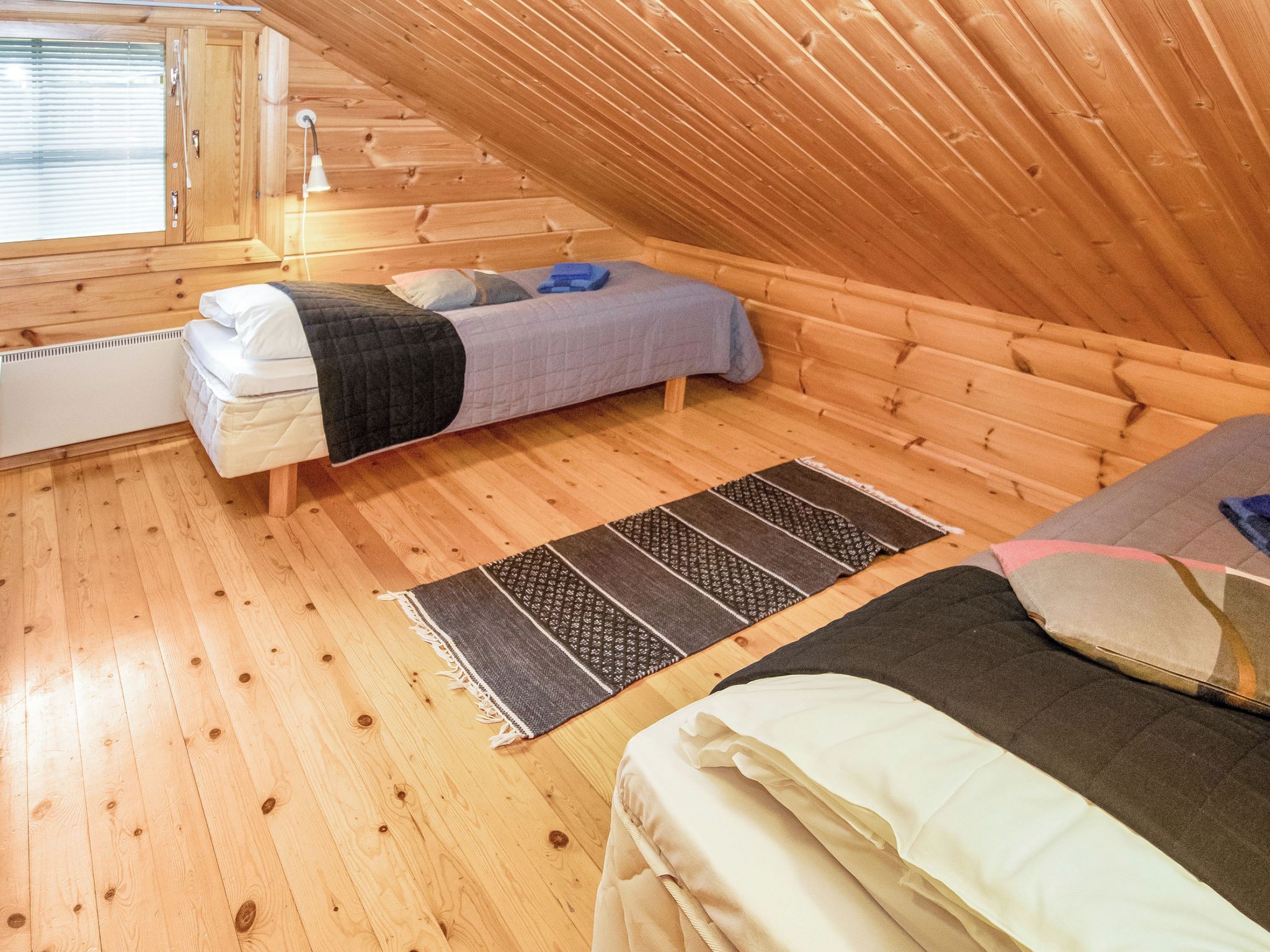 A small, wooden-paneled room with a loft bed, a lower bunk bed, and a window with blinds.
