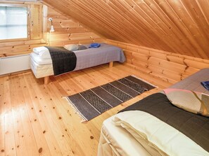 Une petite pièce aux murs lambrés, avec un lit en mezzanine, un lit superposé et une fenêtre équipée de stores.