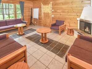 A log cabin interior with a fireplace, wooden furniture, a whiteboard, and a view of the forest through large windows. - Joutsen by Interhome (Loviisa)