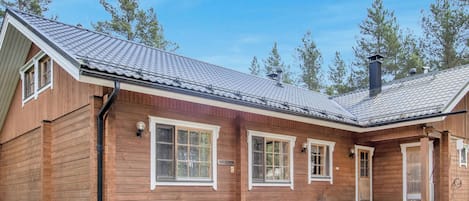 A wooden cabin with a sloped roof, large windows, and a gravel driveway.