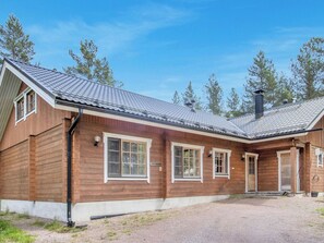 Eine Holzhütte mit geneigtem Dach, großen Fenstern und einer Zuwegung mit Kies.