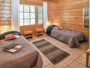 Een kamer in chaletstijl met twee bedden, een bankje, een raam met zonwering en een kleine tafel.