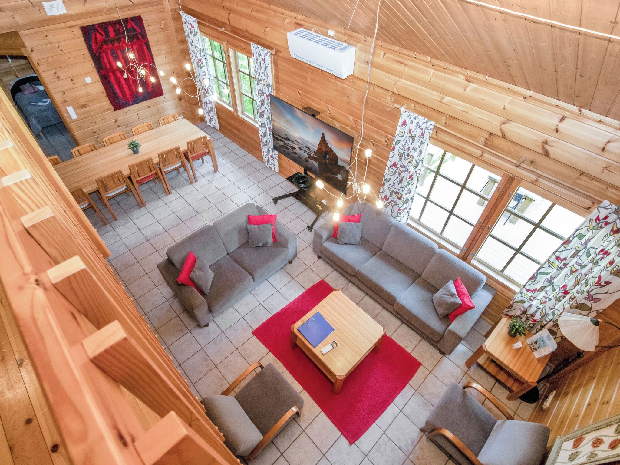 Interior de una cabaña de madera con comedor, sofás, chimenea y ventanas amplias.