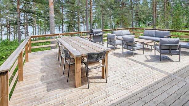 Eine Holzterrasse mit Tisch, Stühlen, einem Grill und einer Sitzecke.