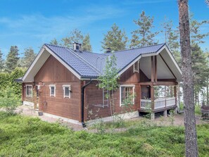 Eine Holzhütte mit Veranda, umgeben von Bäumen und Grünpflanzen.