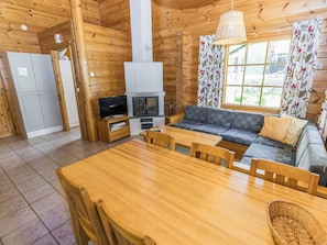 A log cabin interior with a dining area, sofa, television, fireplace, and large windows.