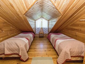 A room with two beds, wooden walls, a sloped ceiling, and a window at the far end.