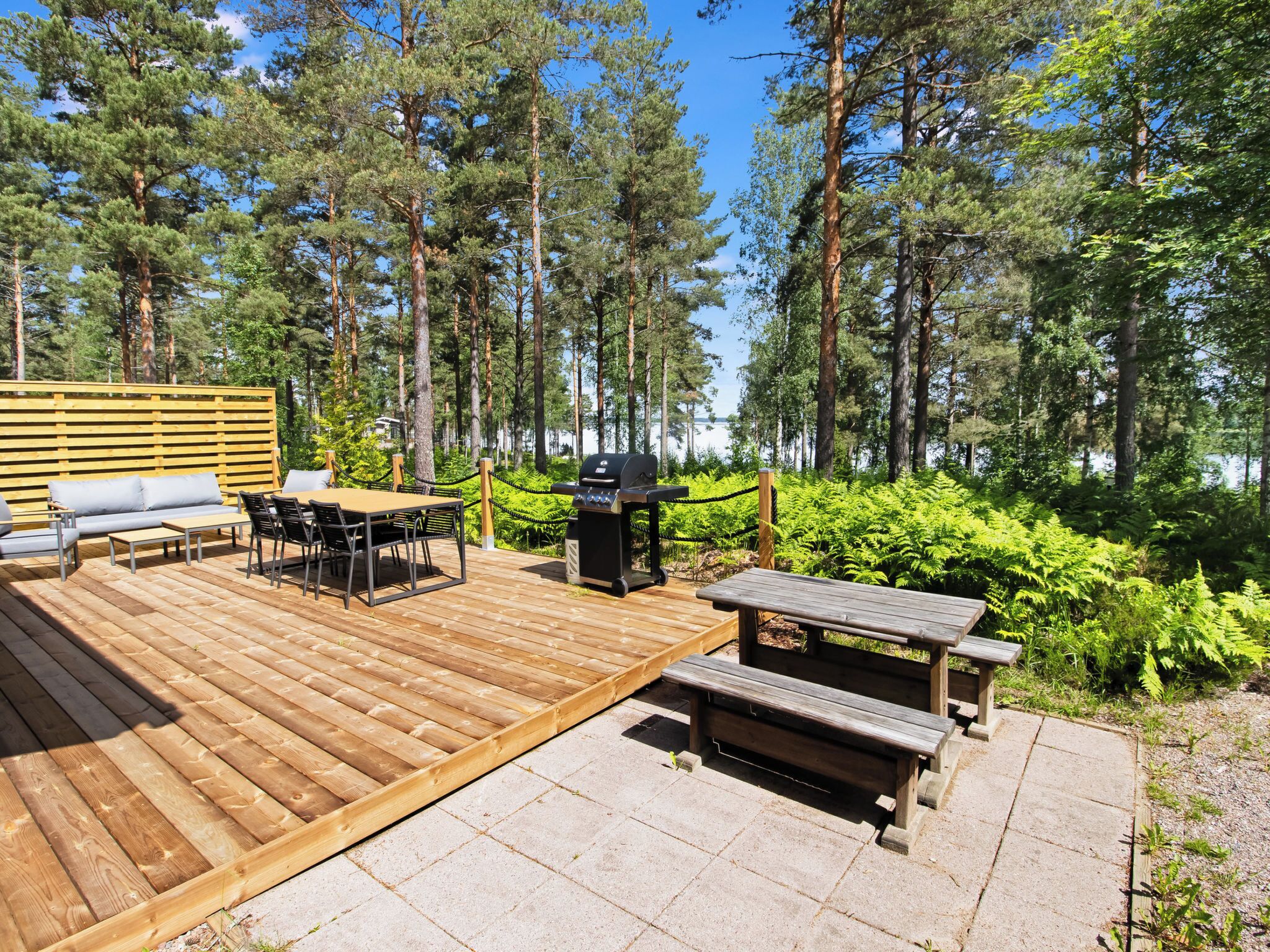 Una terraza con mobiliario exterior, una parrilla y vistas a un bosque y un lago.