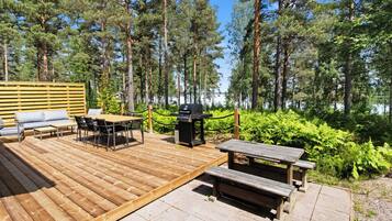 Une terrasse dotée de mobilier d’extérieur, d’un barbecue et offrant une vue sur une forêt et un lac.