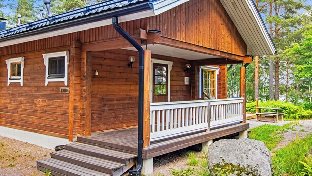 Een houten blokhut met een veranda, trap en schoorsteen.