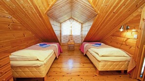 Een knus slaapkamer onder het dak met twee bedden, houten wanden, een schuine kap en een klein raam.