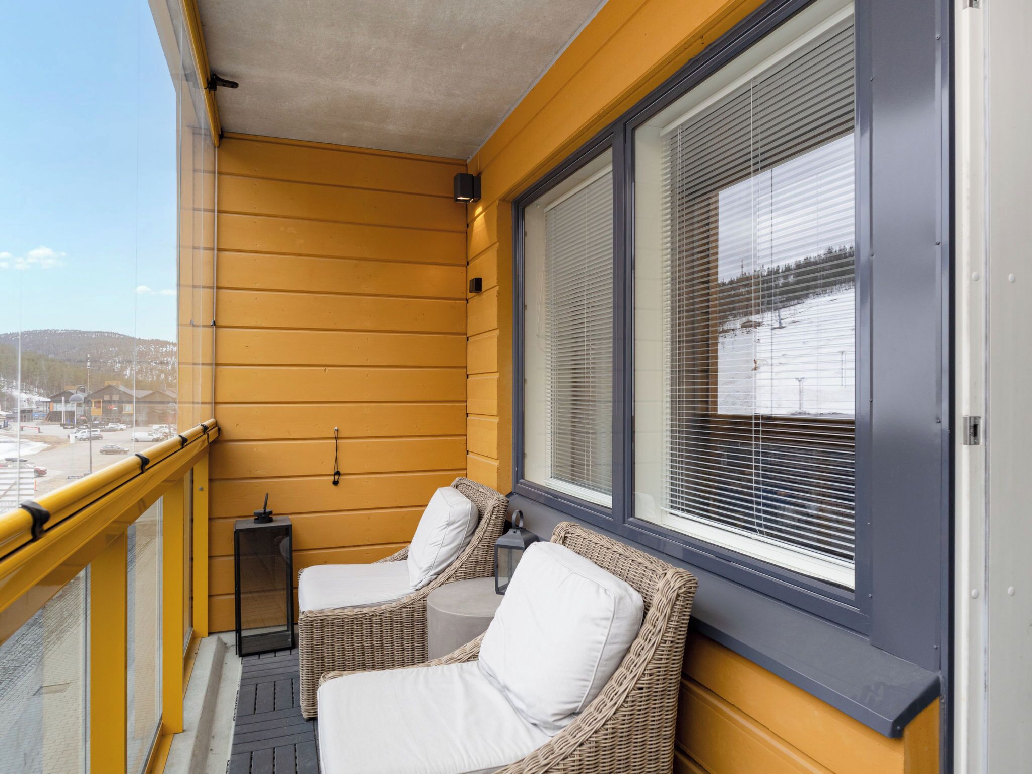 Ein Balkon mit gelben Wänden, zwei Korbstühle mit weißen Kissen und Blick auf eine verschneite Landschaft.