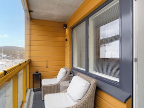 Ein Balkon mit gelben Wänden, zwei Korbstühle mit weißen Kissen und Blick auf eine verschneite Landschaft.