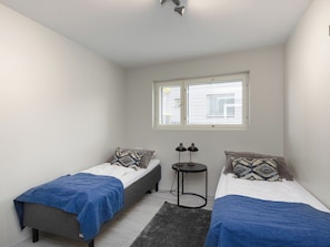 Ein kleines, modernes Schlafzimmer mit zwei Einzelbetten, einem kleinen Tisch und einem Fenster mit Jalousien.