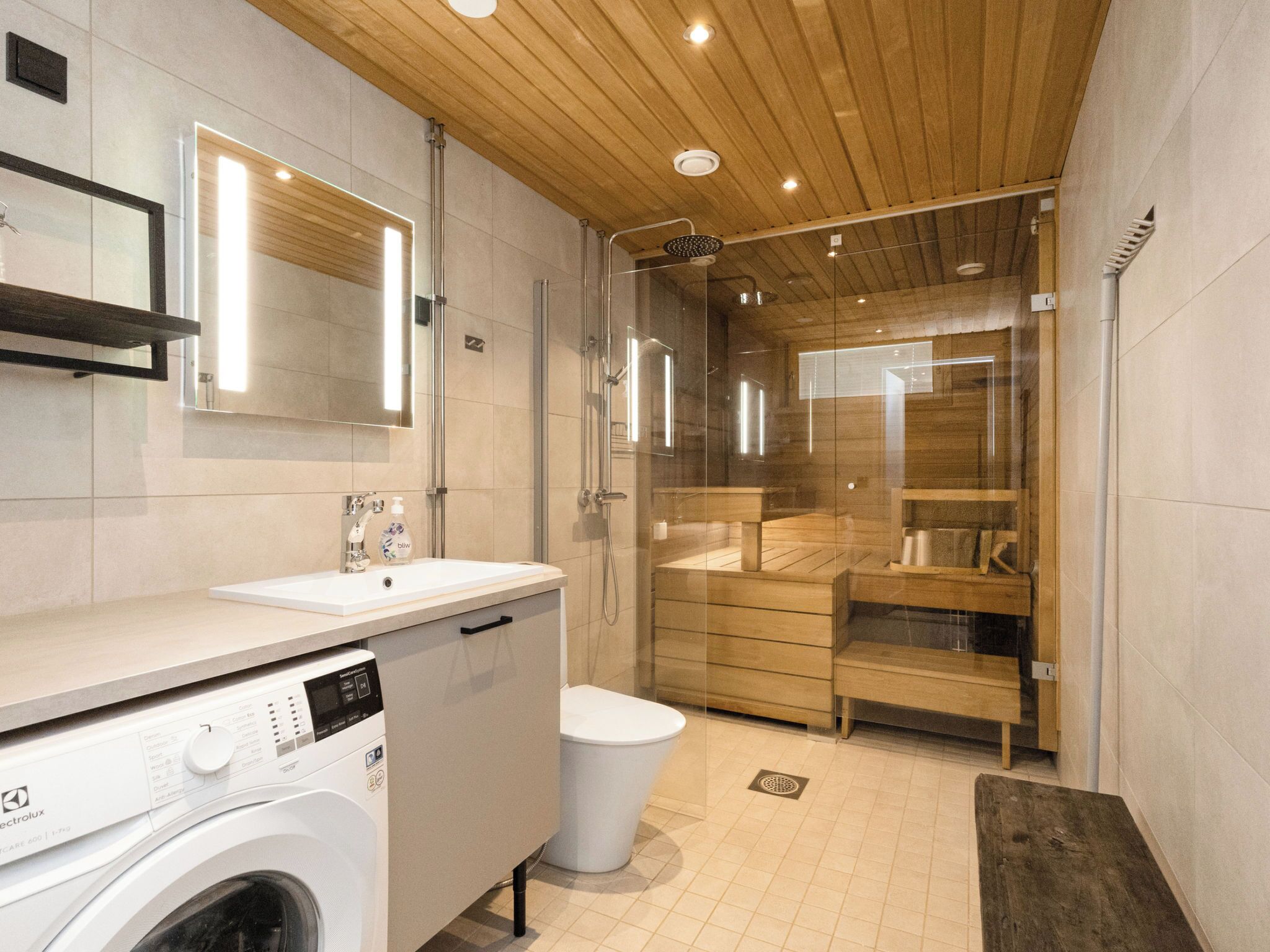 A modern bathroom with a washing machine, a sink, a toilet, and a shower enclosure.