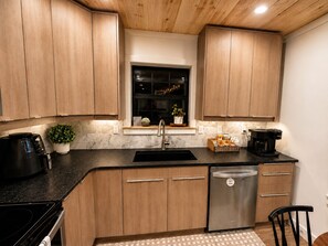 Una cocina moderna con armarios de madera, lavavajillas de acero inoxidable, cafetera y una planta en maceta.