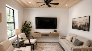 Un soggiorno con TV a schermo piatto, ventilatore a soffitto, divano, una poltrona, tavolino da caffè e una pianta.