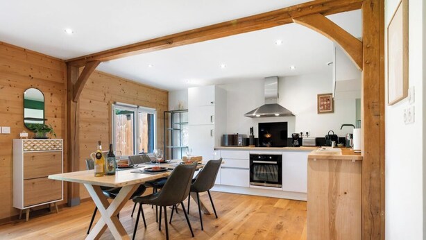 Eine moderne Küche mit Holzbalken, einem Essbereich mit Tisch und Stühlen sowie einem eingebauten Backofen.