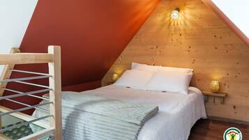 A cozy bedroom with a sloped ceiling, a wooden ladder, a bed with white linens, and two wall-mounted lamps.