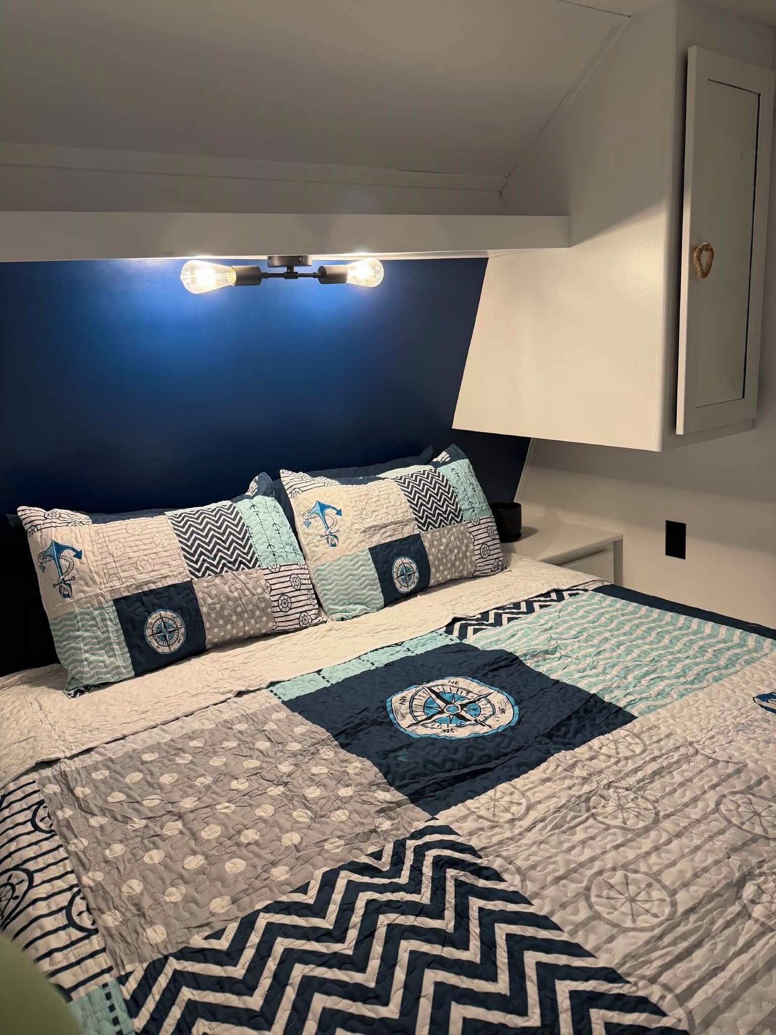 A bedroom with a bed, a headboard, a bedside table, and a wall-mounted lamp.