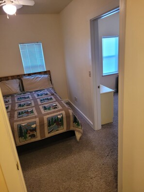 A bedroom with a bed, a window with blinds, a door, and a carpeted floor.
