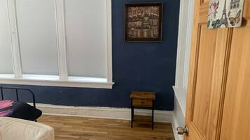 A room with a large window, a small wooden table, a bed with a pillow, and a door.