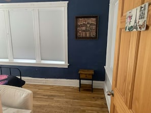 A room with a large window, a small wooden table, a bed with a pillow, and a door.