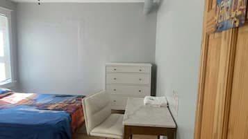 A bedroom with a bed, a desk, a chair, a dresser, and a ceiling fan.