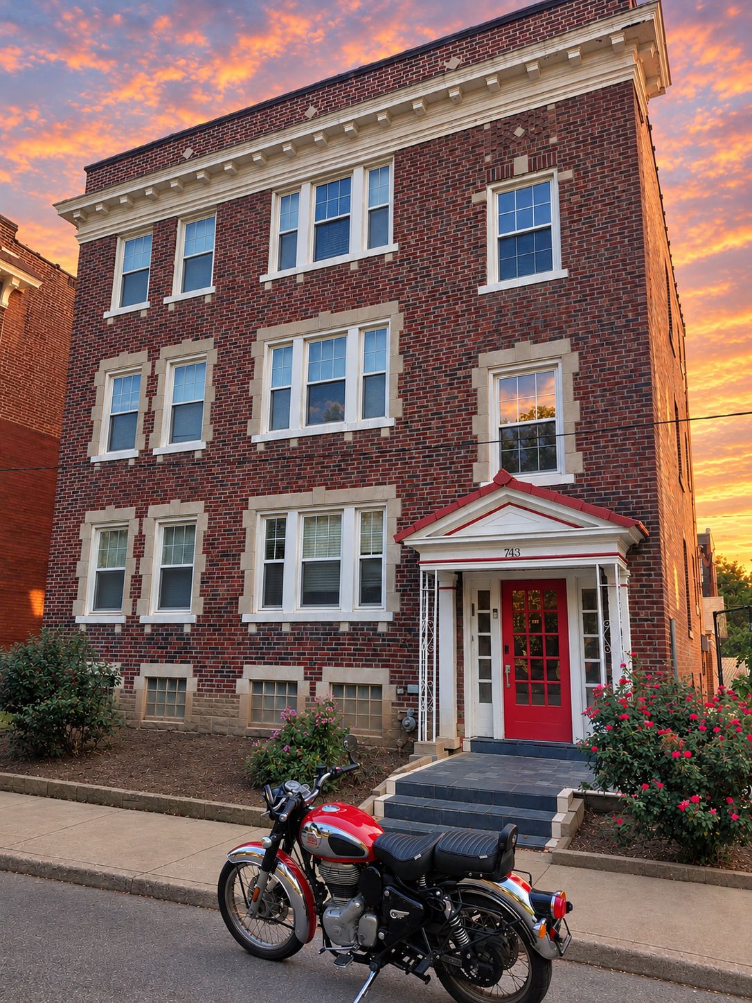 A red brick building with a red door and white trim, a motorcycle parked in front, and a clear sky.