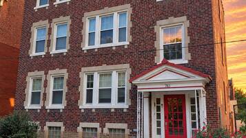 A red brick building with a red door and white trim, a motorcycle parked in front, and a clear sky.