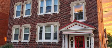 A red brick building with a red door and white trim, a motorcycle parked in front, and a clear sky.