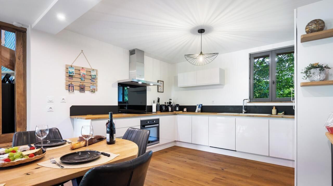 A modern kitchen with white cabinets, a wooden dining table, and a large window.