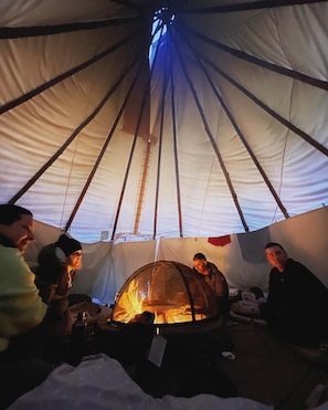 A tent with a central fire, people inside, and a visible tent pole structure. - Chief Joseph, Large Tipi with central firepit (Markdale)