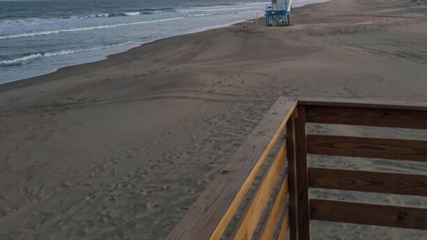 Una playa con una pasarela de madera y una torre de salvavidas a lo lejos.