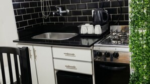 Una cocina compacta con salpicadero de azulejos blanco y negro, un lavabo de acero inoxidable, un hervidor y una estufa.