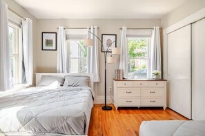 A bedroom with a bed, a dresser, a floor lamp, and a window with curtains. - The Thomas Honeycomb Inn w/ Tiki Bar and Roof Deck (Salem)